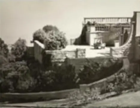 A black and white photo of a building on the side of a hill.