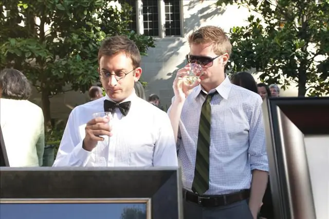 Two men in dress clothes are drinking wine.